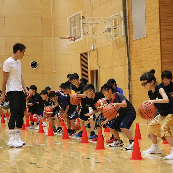 ドリブル練習するココバスのスクール生を見つめる飯島